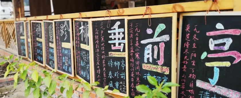 Tableaux noirs avec des inscriptions colorées en caractères asiatiques, accrochés à une structure en bois.