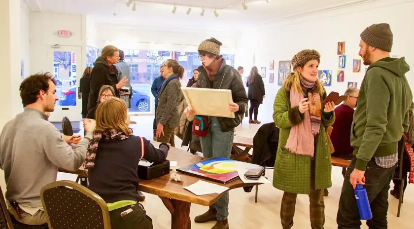 Un groupe de personnes interagissant dans une galerie d'art, avec des œuvres accrochées aux murs.