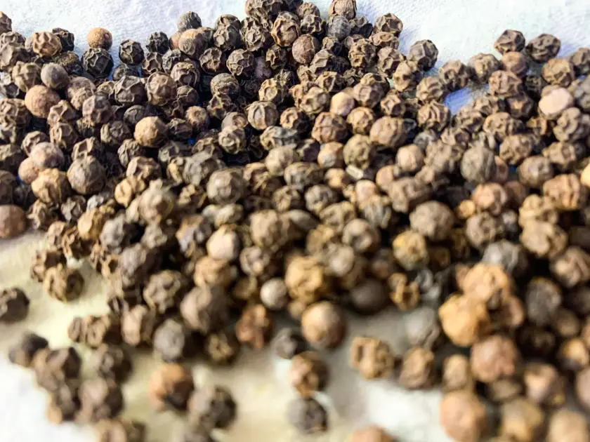Gros plan sur un tas de grains de poivre noir, montrant leur texture rugueuse.