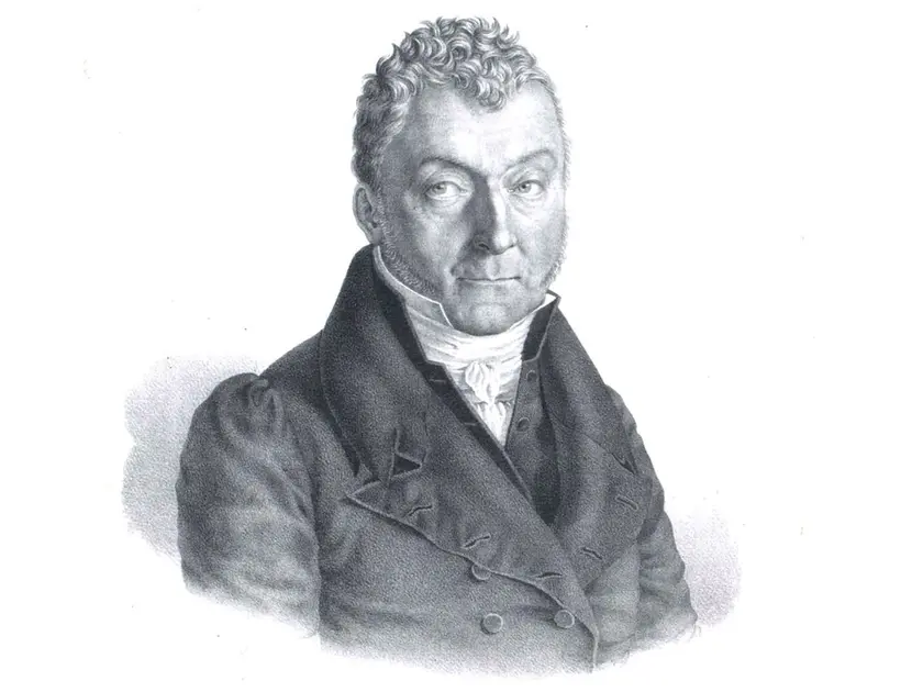 Portrait en noir et blanc d'un homme au visage sérieux, portant un manteau et une chemise à col.