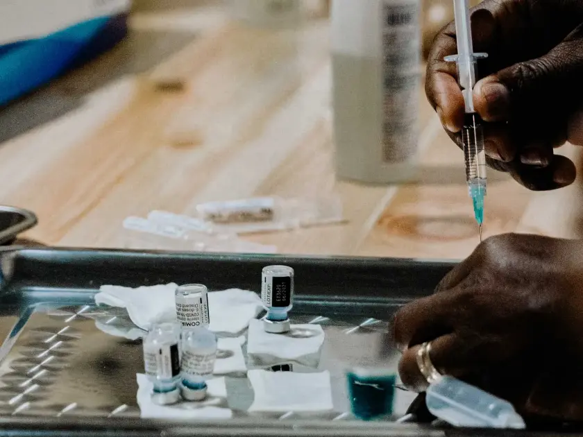 Une main prépare une seringue avec un flacon de vaccin sur une surface en métal.