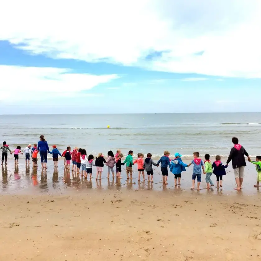 Groupe d'enfants tenant la main, formant une chaîne sur la plage, face à la mer.