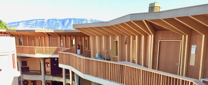 Vue d'un bâtiment moderne en bois avec balcons, entouré de montagnes.