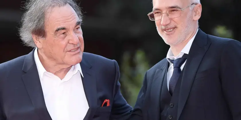 Deux hommes en costume se saluent avec un sourire, dans un cadre extérieur.