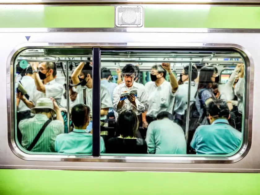 Intérieur d'un métro bondé avec des passagers en chemises blanches et masques, un homme au centre regarde son téléphone.