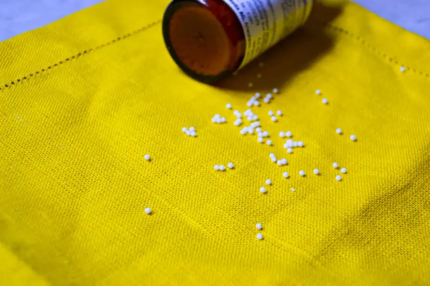 Des billes blanches éparpillées sur un tissu jaune, avec un flacon renversé à côté.