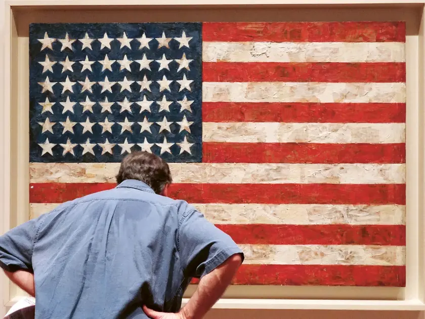 Un homme observe une œuvre d'art représentant le drapeau américain, avec des étoiles blanches sur fond bleu et des bandes rouges et blanches.