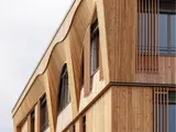 Façade d'un bâtiment moderne en bois avec des motifs architecturaux ondulés et des fenêtres encadrées.