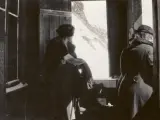 Deux personnes à l'intérieur d'un bâtiment, regardant par une fenêtre ouverte vers un paysage montagneux.