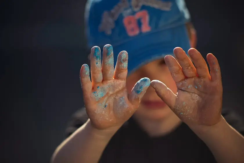 Un enfant avec un chapeau bleu montre ses mains couvertes de peinture.