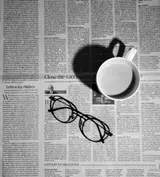 Une tasse de café posée sur un journal, avec des lunettes à côté.