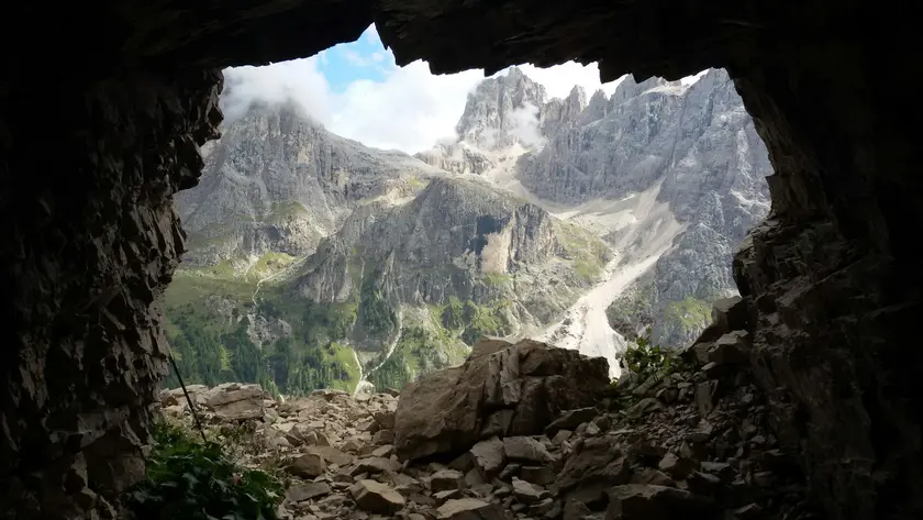 Vue d'une montagne à travers l'ouverture d'une grotte, avec des nuages et des rochers.