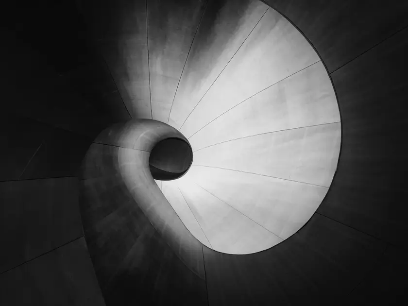 Vue en noir et blanc d'une spirale architecturale en béton, éclairée par une source de lumière centrale.