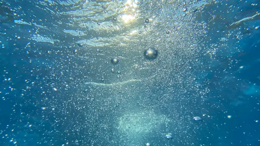 Vue sous-marine montrant des bulles d'air dans l'eau avec des reflets de lumière.